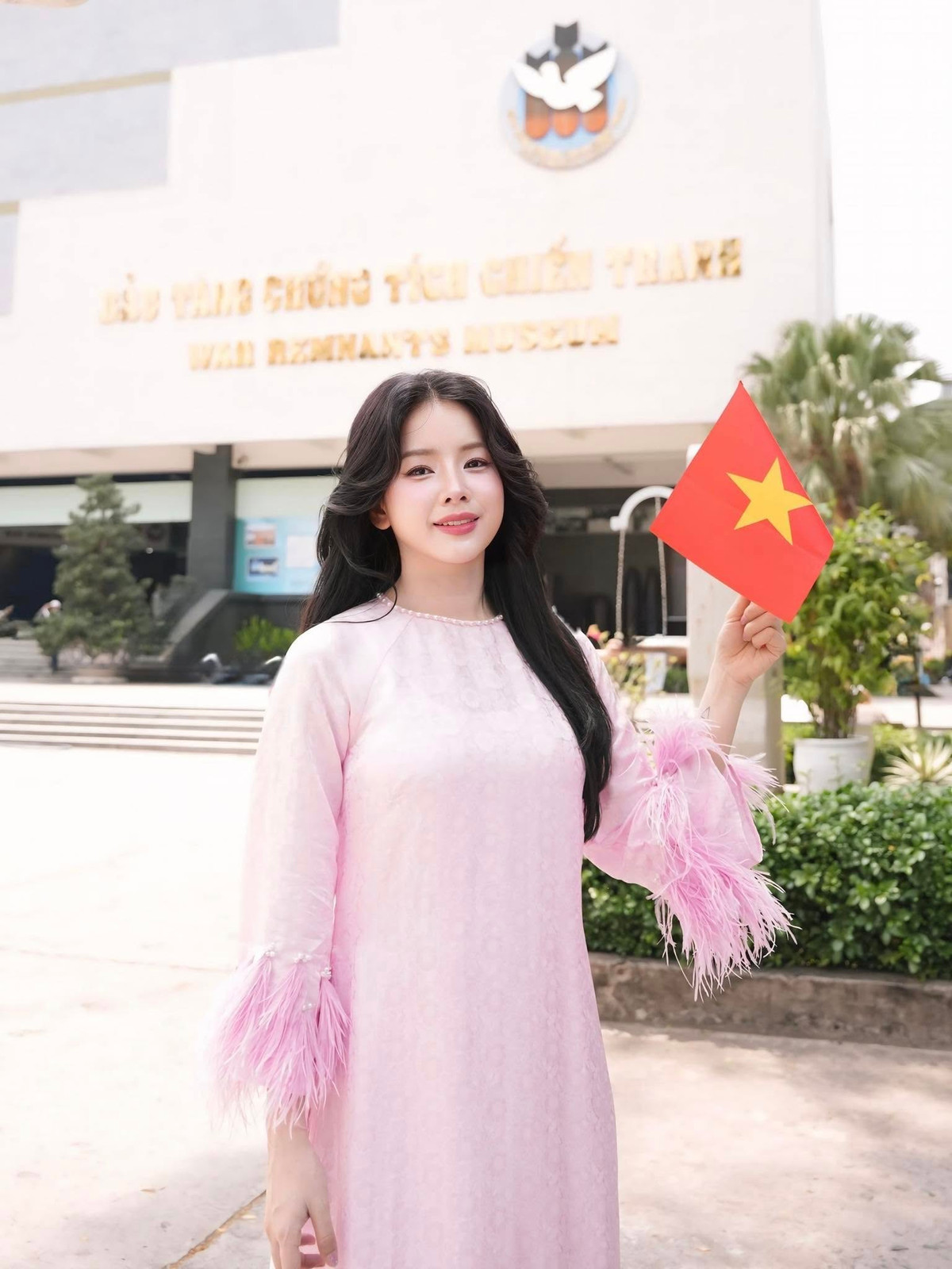 Nữ DJ cầm lá cờ đỏ sao vàng nhỏ nhắn trên tay, tạo dáng trước các hiện vật lịch sử tại Bảo tàng Chứng tích Chiến tranh, nơi lưu giữ những dấu ấn hào hùng của dân tộc trong thời kỳ kháng chiến. Khung cảnh trang nghiêm kết hợp với nét đẹp hiện đại của Mie tạo nên sự giao thoa đặc biệt giữa truyền thống và thế hệ trẻ hôm nay.