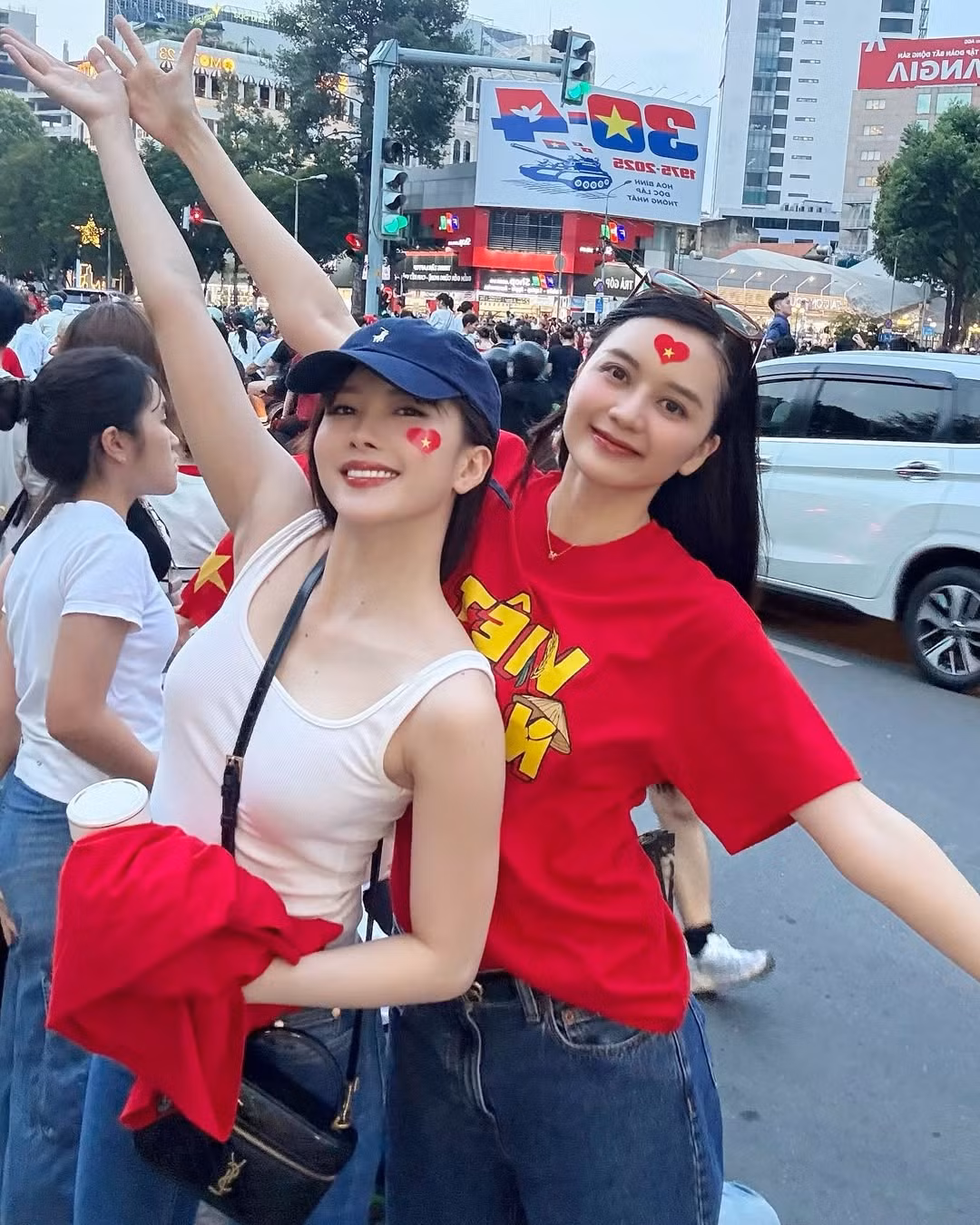 Diện áo thun đỏ in dòng chữ "Việt Nam" nổi bật, cả hai nhanh chóng hòa mình vào không khí hân hoan đang dâng trào giữa lòng thành phố.