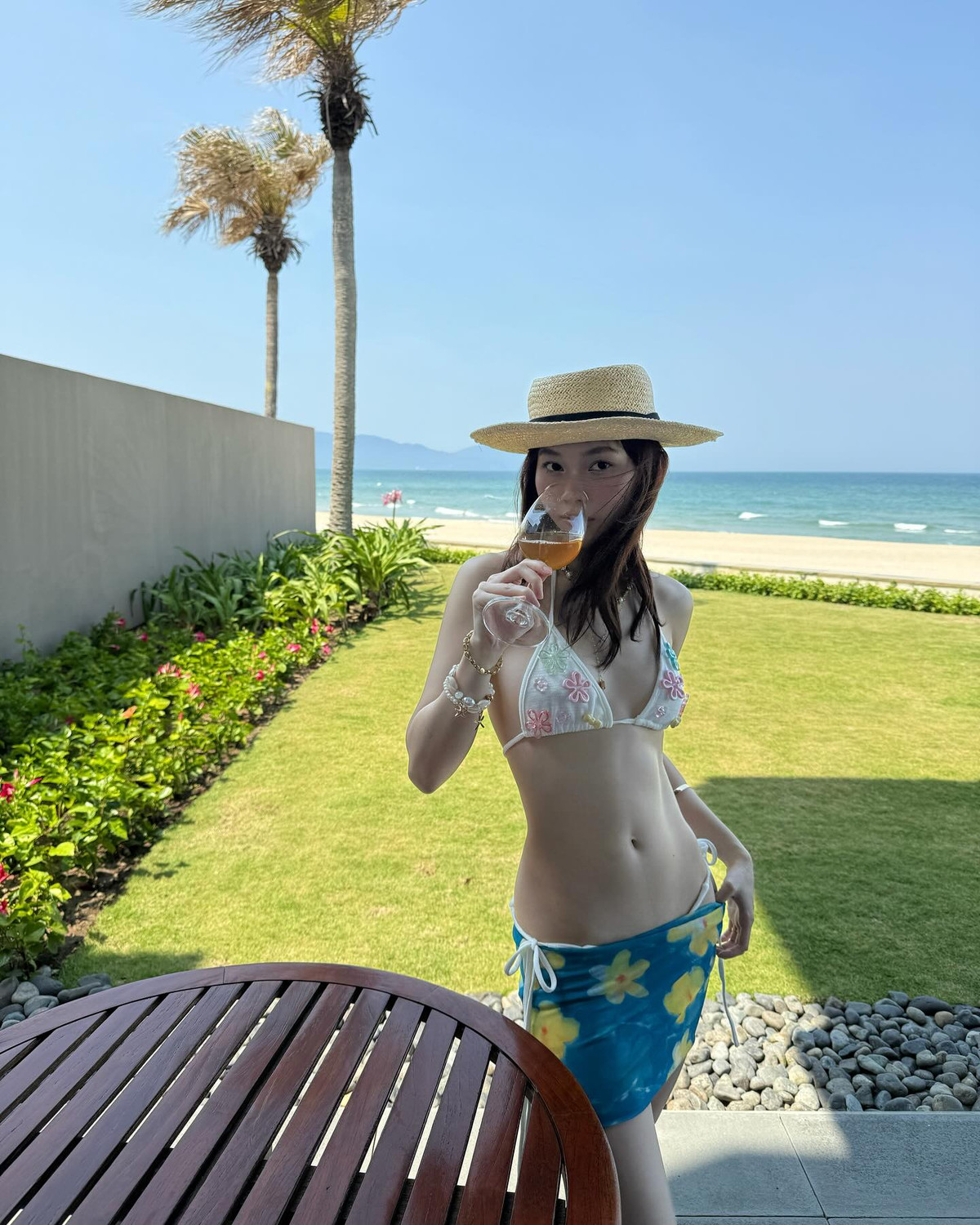 Không chỉ gây sốt với visual rạng rỡ và thân hình cuốn hút, Ly Phạm còn cho thấy gu thời trang tinh tế khi chọn lựa trang phục và phụ kiện vô cùng ăn ý. Bộ bikini trắng với họa tiết hoa nổi bật mang phong cách Y2K, vừa dễ thương vừa gợi cảm, kết hợp cùng chân váy quấn hoa vàng tạo nên tổng thể rực rỡ, trẻ trung, đúng chuẩn “hot girl mùa hè”.