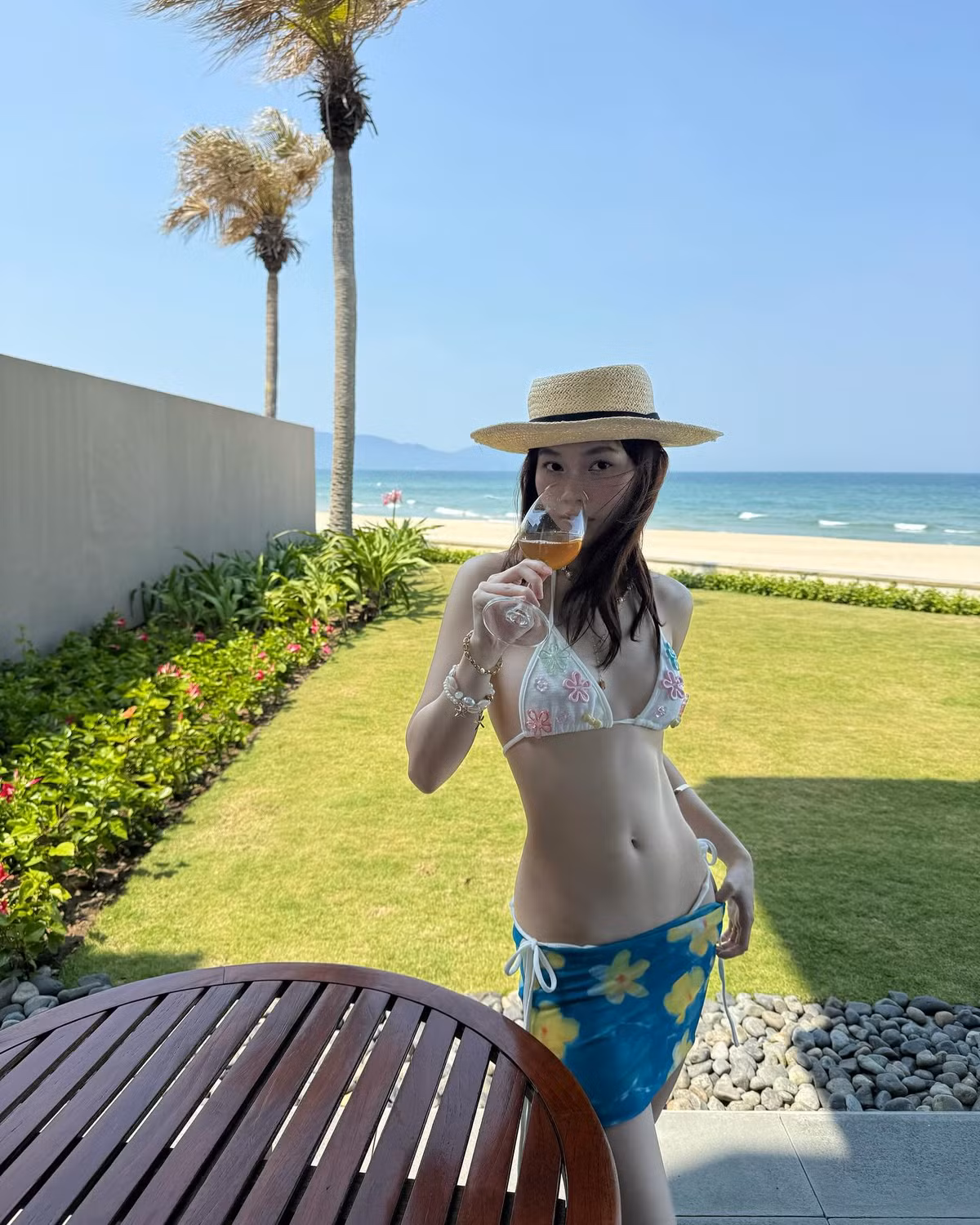 Không chỉ gây sốt với visual rạng rỡ và thân hình cuốn hút, Ly Phạm còn cho thấy gu thời trang tinh tế khi chọn lựa trang phục và phụ kiện vô cùng ăn ý. Bộ bikini trắng với họa tiết hoa nổi bật mang phong cách Y2K, vừa dễ thương vừa gợi cảm, kết hợp cùng chân váy quấn hoa vàng tạo nên tổng thể rực rỡ, trẻ trung, đúng chuẩn “hot girl mùa hè”.