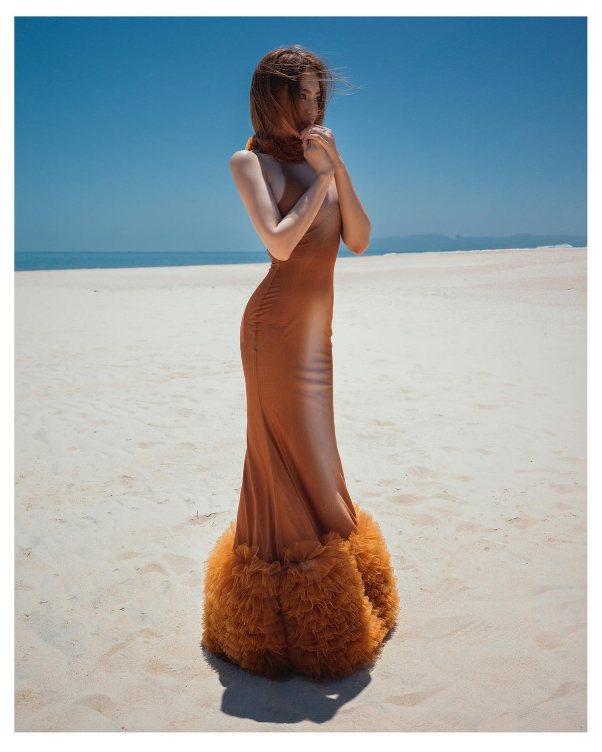 Chiếc váy ôm sát màu nâu cháy hòa quyện với làn da trắng ngần, làm nổi bật đường cong “vòng nào ra vòng nấy” của Lan Ngọc. Phần cổ váy được tạo điểm nhấn bằng chi tiết lông mềm mại màu cam đất, vừa cổ điển vừa cá tính, tạo nét quý phái rất riêng.