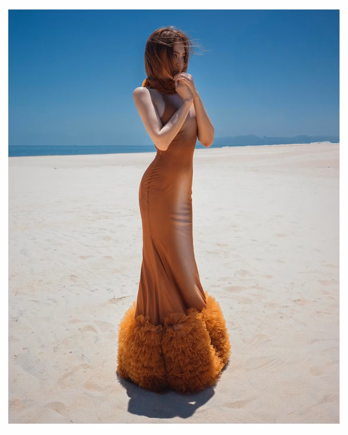 Chiếc váy ôm sát màu nâu cháy hòa quyện với làn da trắng ngần, làm nổi bật đường cong “vòng nào ra vòng nấy” của Lan Ngọc. Phần cổ váy được tạo điểm nhấn bằng chi tiết lông mềm mại màu cam đất, vừa cổ điển vừa cá tính, tạo nét quý phái rất riêng.