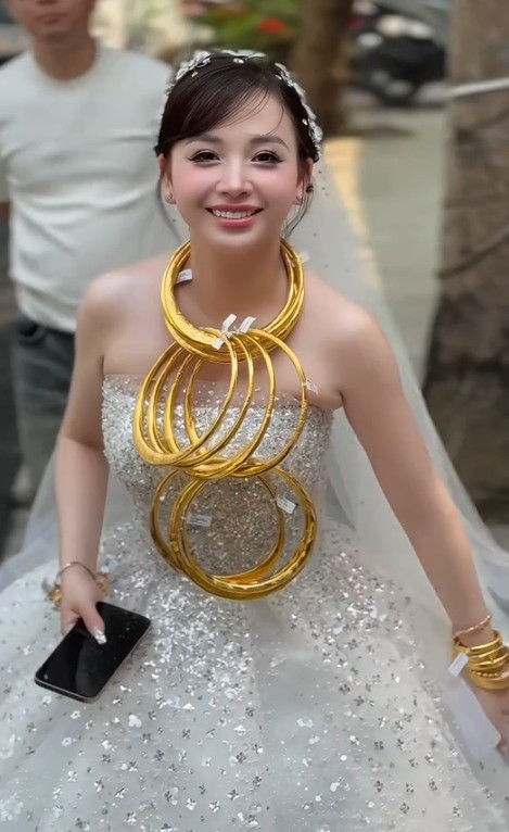 Trong bộ váy cưới trắng cúp ngực, cô dâu trẻ khoe sắc rạng ngời. Nhưng điều khiến tất cả mọi ánh mắt đổ dồn không chỉ là nhan sắc xinh đẹp, mà chính là loạt vòng vàng được đeo kín từ cổ, tay đến ngón tay. (Ảnh: Chau Toc Nau)