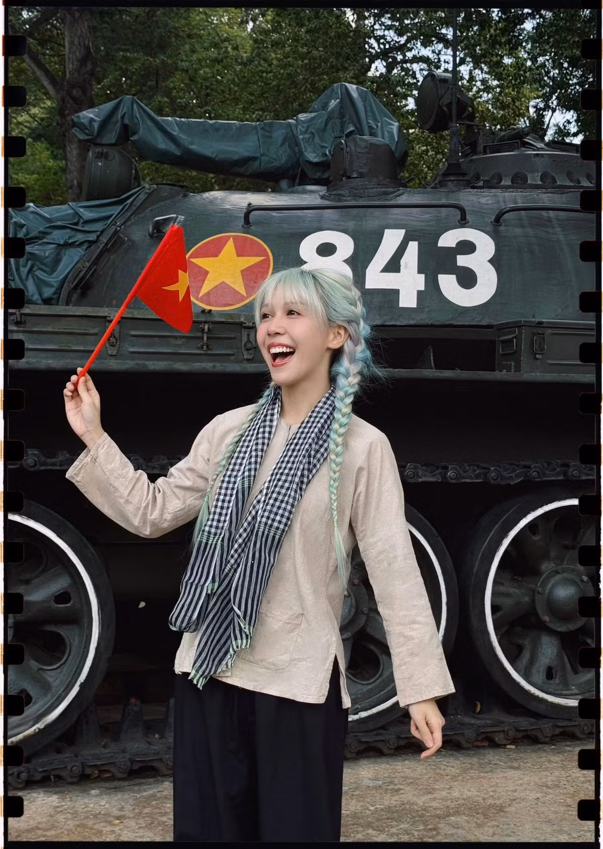 Diện trang phục truyền thống giản dị với áo bà ba, quần đen rộng, khăn rằn và mái tóc tết bím tinh nghịch, Hậu Hoàng xuất hiện bên chiếc xe tăng huyền thoại số 843 - biểu tượng lịch sử gắn liền với ngày giải phóng miền Nam - mang đến hình ảnh mộc mạc nhưng giàu tính biểu tượng.