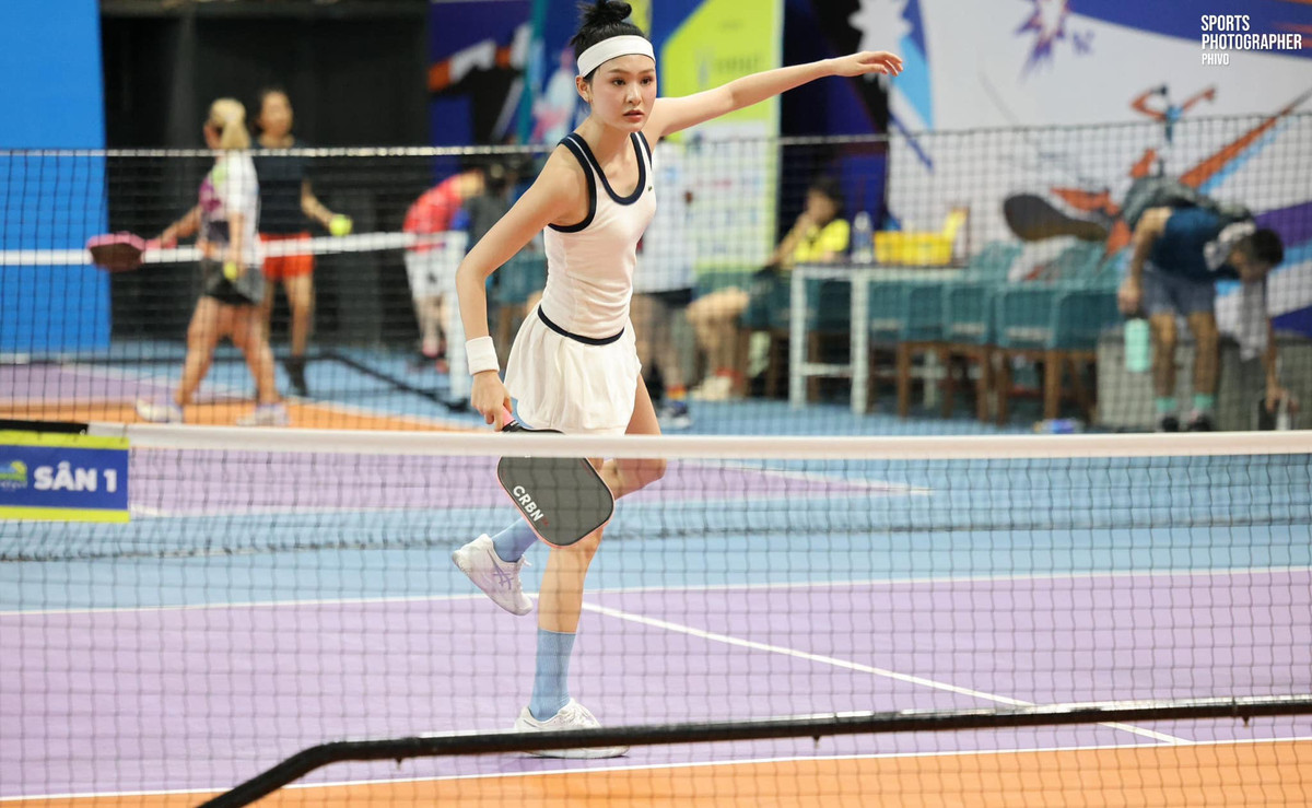 Thiết kế cổ xẻ sâu và phần xếp ly tinh tế giúp tăng độ nữ tính nhưng không kém phần thể thao. Cô mix cùng giày Asics trắng, tất cổ cao và băng đô đồng màu – tạo tổng thể “chuẩn vận động viên chuyên nghiệp” nhưng vẫn mang nét thời trang runway.