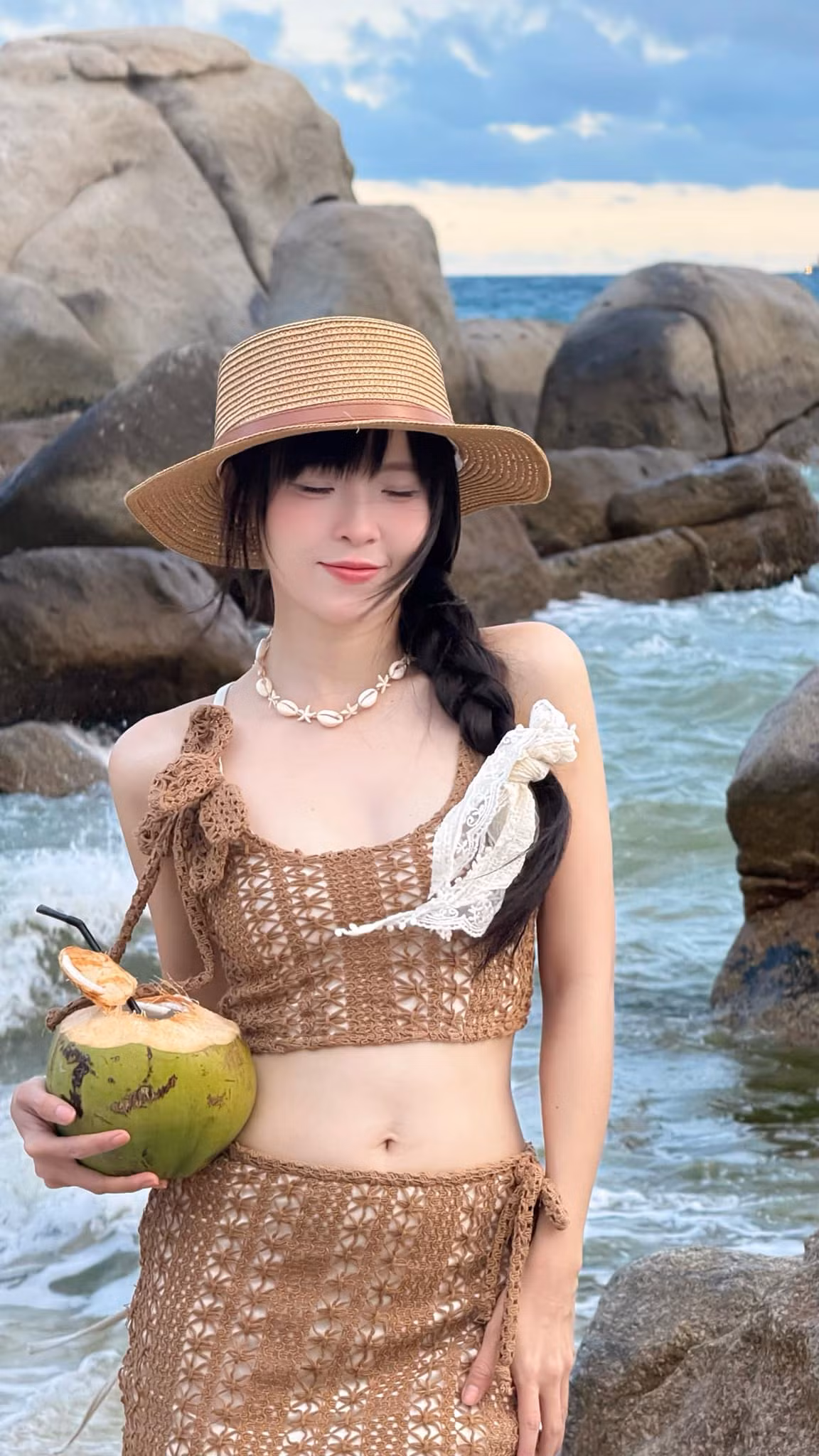 Chi tiết hoa móc nổi ở vai áo là điểm nhấn nhẹ nhàng nhưng tinh tế, tôn lên vẻ nữ tính. Chiếc chân váy ngắn được buộc dây bên hông không chỉ tôn dáng mà còn mang đến cảm giác phóng khoáng, tự do đúng chất du lịch biển.