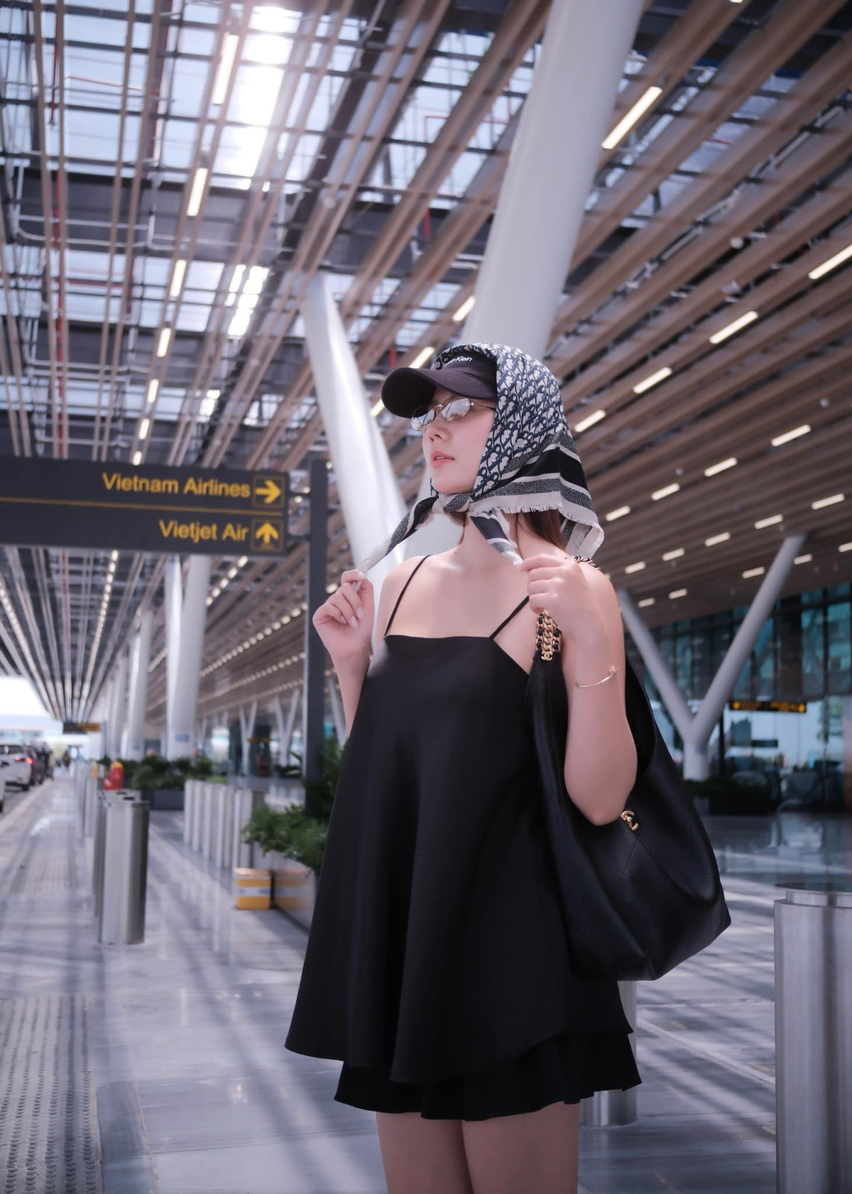 Điểm nhấn bất ngờ chính là chiếc khăn turban họa tiết Dior nàng cựu hot girl ứng dụng, kết hợp cùng mũ lưỡi trai đen basic. Sự pha trộn giữa nét cổ điển và hiện đại tạo nên vẻ ngoài cá tính, lạ mắt nhưng không kém phần sang chảnh. Đây cũng là combo phụ kiện thường thấy trong phong cách "travel chic" của các fashionista quốc tế.