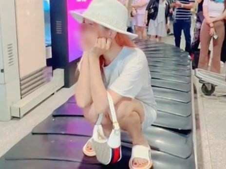 Cụ thể, cô gái này đã ngồi hẳn lên băng chuyền hành lý khi nó vẫn đang hoạt động, xung quanh là nhiều hành động đang đứng chờ lấy hành lý.