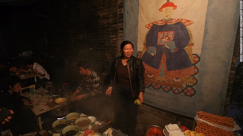 Người phụ nữ bán hàng rong trên phố. Phía sau là một bức tranh vẽ một viên quan thời nhà Thanh.