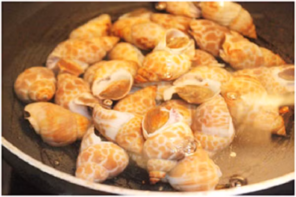 Đầu tiên bạn rửa sạch ốc hương qua vài lần nước rồi ngâm ốc vào trong nước vo gạo để ốc nhả hết bùn đất. Sau đó cho ốc hương vào luộc sơ rồi đổ ra rổ cho ráo nước. (Ảnh: 123amthuc.com)