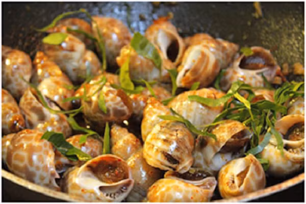 Cuối cùng bạn tắt bếp, rắc một ít lá chanh lên bề mặt ốc, dùng đũa đảo đều, múc ra đĩa dùng nóng cùng cơm hay nhâm nhi với chút bia lạnh sẽ rất tuyệt. (Ảnh: 123amthuc.com)