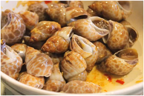 Cho ốc vào bát to, thêm nước mắm đã pha tỏi ớt vào, trộn đều, ướp ốc hương khoảng 15 phút để gia vị ngấm đều. (Ảnh:123amthuc.com)