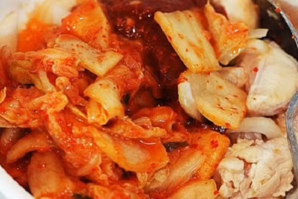 Đến khi thịt vừa săn lại, bạn cho hành tây, kimchi và sốt Gochujang vào đảo nhanh tay cho kim chi ngấm gia vị từ thịt và thịt có màu của kim chi cho ngon mắt. Cho vào nồi khoảng 300ml nước lọc, đun to lửa đến khi sôi. (Ảnh: toinayangi.com) 