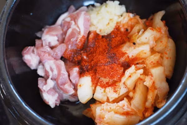 Nguyên liệu: Kim chi hàn Quốc, thịt lợn, cải thảo, đậu phụ, hành lá, hành tây, tỏi, nước sốt Gochujang và gia vị mắm, hạt nêm, tiêu, dầu. Đầu tiên bạn thái khúc kim chi, rửa sạch thịt, thái miếng vừa ăn, hành lá và hành tây rửa sạch, hành tây bổ múi cau, tỏi băm nhuyễn. (Ảnh: eva.vn)