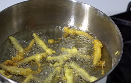 Trộn hỗn hợp nước sốt gồm: nước tương + đường + ớt rồi cho vào chảo đun sôi. Thả phần hoa chuối đã chiên vào đảo đều cho gia vị áo đều từng chiếc hoa chuối chiên rồi rưới thêm chút dầu ăn. Ảnh: bepgiadinh