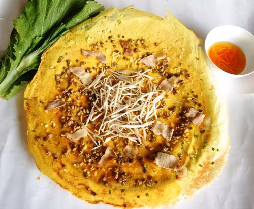 Ốc gạo, thịt trắng đục, béo thơm được rải đều trong lòng bánh. Bắc chảo lên và xoay vòng một cách nhẹ nhàng cho bột tráng đều thành một hình tròn, mép bánh không bị rách. Thêm củ sắn (củ đậu) xắt sợi và giá thêm vị ngọt cho bánh, làm cho bánh xèo ốc gạo ăn không ngấy. Ảnh: bepgiadinh