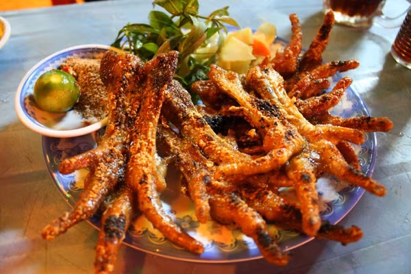 Chân gà, cánh gà nướng. Chân gà nướng là món ăn vặt được nhiều người yêu thích vì khi nướng lên thịt gà có vị thơm ngon thấm gia vị. Những cặp chân gà nướng vàng rộm thơm ngon khiến thực khách khó lòng từ chối. Cầm chiếc chân gà, chấm vào chén muối tiêu đưa lên miệng, thưởng thức với một ít đồ chua, miếng xôi chiên, món ăn là sự tổng hợp các vị giòn, chua, dẻo thơm sẽ rất tuyệt. (Ảnh: 7monngonmoingay.net)