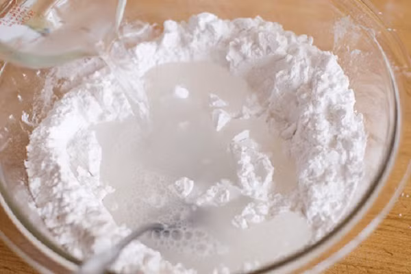 Đầu tiên cho bột vào nước cùng các thành phần khác như: muối, dầu ăn, men nở. Dùng tay nhào thật kĩ bột và các nguyên liệu trên, nhào đến khi thấy bột không còn dính tay nữa là được. Để tránh cho bột bị dính và vón cục, bạn nhào trước các nguyên liệu khô với dầu ăn rồi từ từ cho nước vào. (Ảnh: sdwingnuts.com)