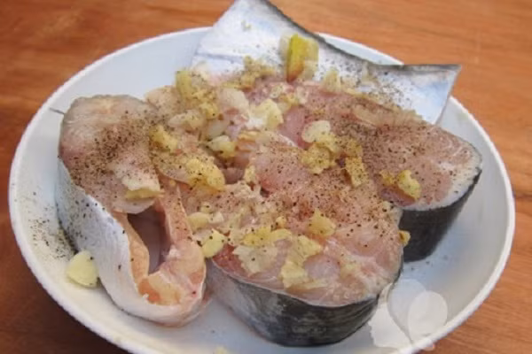  Đầu tiên cá đem làm sạch, cạo bớt lớp vảy bên ngoài để cá ngon hơn. Chặt cá thành các khúc vừa đẹp mắt, đem ướp với ít muối, hạt tiêu, nước mắm cho ngấm gia vị. Thêm ít riềng giã ướp khoảng 20 phút cho thịt cá thấm đều. (Ảnh: vaobepnauan.com)