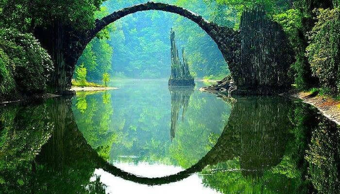 3. Cây cầu Die Rakotzbrück Cây cầu Die Rakotzbrück được xây dựng vào thế kỷ 19 ở Đức nổi tiếng với độ chính xác độc đáo. Trên hồ nước, cây cầu và sự phản chiếu của nó hợp nhất thành một vòng tròn đá hoàn chỉnh và hoàn hảo, bất kể bạn nhìn thấy nó từ đâu. Có lẽ đây là lý do tại sao cây cầu còn được gọi là Cầu Devil. Có vẻ như các nhà kiến trúc xây cây cầu nhấn mạnh vào tính thẩm mỹ của nó hơn là tiện ích của nó. Cả hai đầu của Rakotzbrücke đều có các đỉnh đá mỏng được lắp đặt, để làm cho nó trông giống như các cột đá bazan tự nhiên, thường thấy ở nhiều vùng của Đức.