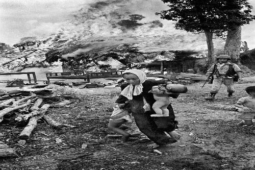 Một người phụ nữ Việt Nam bế trên tay cậu con nhỏ và kéo theo một cô con gái, vội vàng chạy ra khỏi ngôi nhà đang bốc cháy. (Ảnh AP).