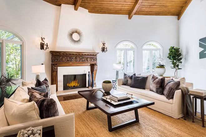 Phòng khách thoáng mát, ngập tràn ánh sáng tự nhiên từ những ô cửa sổ hình vòm. Lò sưởi với khung gỗ được chạm khắc tinh xảo khiến căn phòng trở nên sang trọng hơn.
