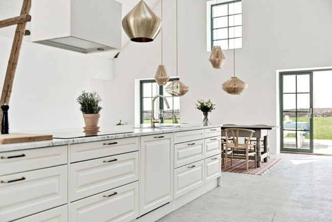 Nhà bếp có đảo bếp và tủ bếp sơn màu trắng đơn sắc phía trên có giếng trời hút ánh sáng.