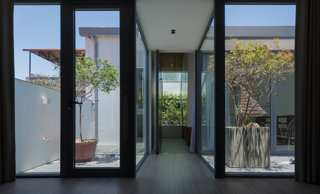 Cửa kính tạo thành một khoảng ban công nhỏ nhìn ra khu phố, mang đến sự thông thoáng cho căn phòng. Cửa kim loại đục lỗ cho ánh sáng hắt vào nhà vừa đủ mà vẫn giữ được sự riêng tư cần thiết. Phần trần nhà được ốp thêm các tấm gỗ ép vừa tạo thẩm mỹ vừa giúp không gian cao, thoáng hơn, đồng thời giảm tải nhiệt cho không gian bên dưới vào những ngày nắng nóng.