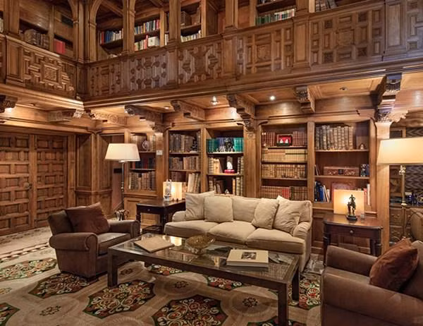 Căn nhà có cả một thư viện hai tầng mở rộng với các ô đựng sách được chạm khắc bằng tay tinh tế. Đồ nội thất sang trọng, với tông vàng ấm chạy dài cả căn phòng.