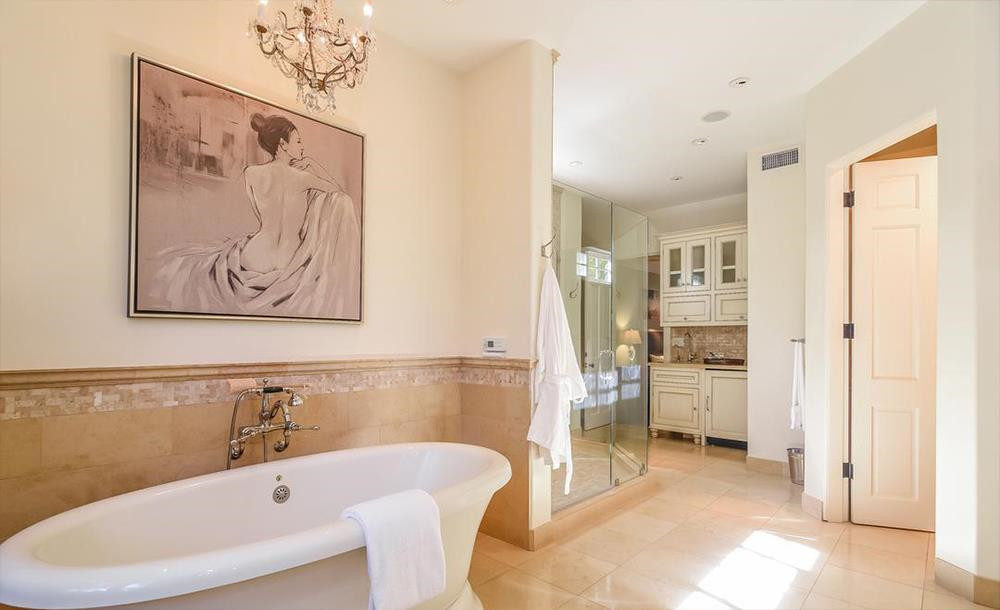 Phòng tắm chính sang trọng được thiết kế uốn khúc với nền gạch màu be, bên cạnh phòng giặt ủi. Tại đây còn có quầy bar thu nhỏ giúp gia chủ có thể vừa ngâm mình trong bồn nước, vừa thưởng thức các đồ uống.