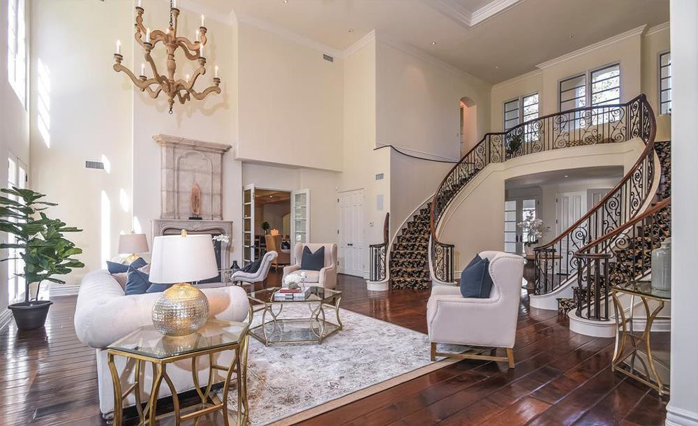 Phòng khách được kết nối trực tiếp với tiền sảnh, có những điểm nhấn như đèn chùm, những ô cửa sổ rộng lớn, lò sưởi bằng đá được chạm khắc tinh xảo, và đặc biệt là cặp cầu thang uốn lượn dẫn lên tầng 2.