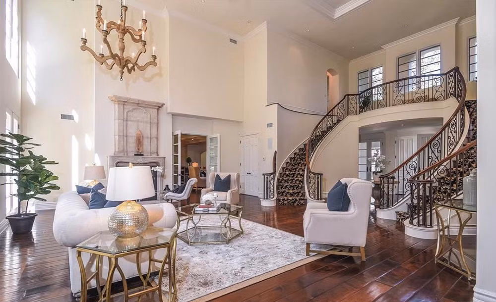 Phòng khách được kết nối trực tiếp với tiền sảnh, có những điểm nhấn như đèn chùm, những ô cửa sổ rộng lớn, lò sưởi bằng đá được chạm khắc tinh xảo, và đặc biệt là cặp cầu thang uốn lượn dẫn lên tầng 2.