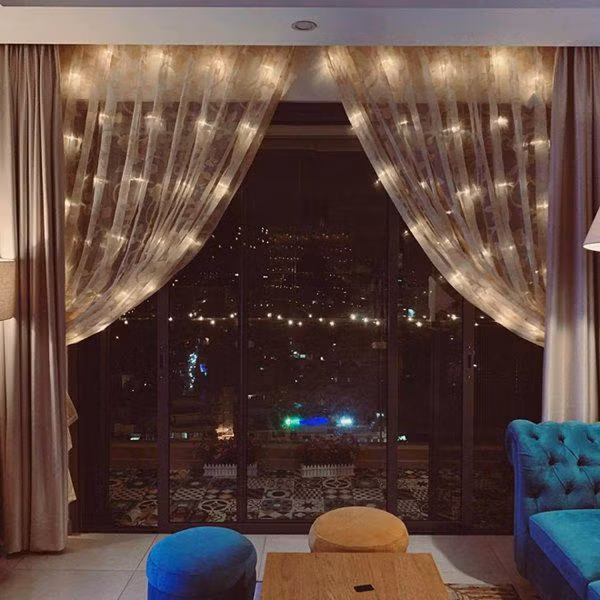 Theo đó, bên trong căn hộ của Nam Cường trang trí nhiều loại đèn khác nhau vô cùng lấp lánh đặc biệt là khi về đêm. Nam ca sĩ cũng lựa chọn những đồ vật nhỏ nhưng vô cùng đáng yêu để đặt ở phòng khách. Để Tết thêm rực rỡ Nam Cường đặt một cây hoa đào trong phòng khách, bên cạnh đặt thêm cây đào phai giả treo đầy lời chúc, lì xì may mắn đầu năm. Phía ngoài anh cũng đặt thêm những chậu hoa nhỏ đẹp mắt.