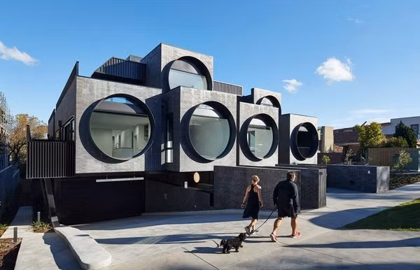 Dự án được thiết kế bởi các kiến trúc sư thuộc công ty kiến trúc BKK tọa lạc tại một khu dân cư cách trung tâm thành phố khoảng 10km về phía đông bắc, thuộc Melbourne, Úc. Công ty kiến trúc BKK Architects đã thiết kế 44 căn hộ nằm trên sườn dốc với sáu ô cửa sổ lớn gắn trên các khối hộp bê tông đặt so le. Kiểu thiết kế này khiến các khối hộp có hình dạng như một chiếc máy ảnh, điều này cũng mang ý nghĩa các nhà thiết kế mong muốn các ô cửa này sẽ giống như các ống kính giúp gia chủ có thể ngắm nhìn không gian bên ngoài.