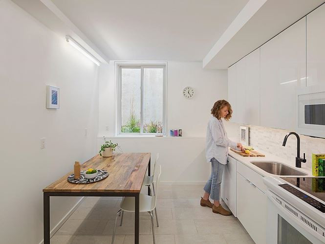 Nhà bếp được thiết kế với gam màu trắng và sàn lát gạch để tạo ra không gian gọn gàng, ngăn nắp. Vì diện tích nhà khá hẹp nên nội thất như bàn ăn và bồn rửa được lựa chọn rất đơn giản.