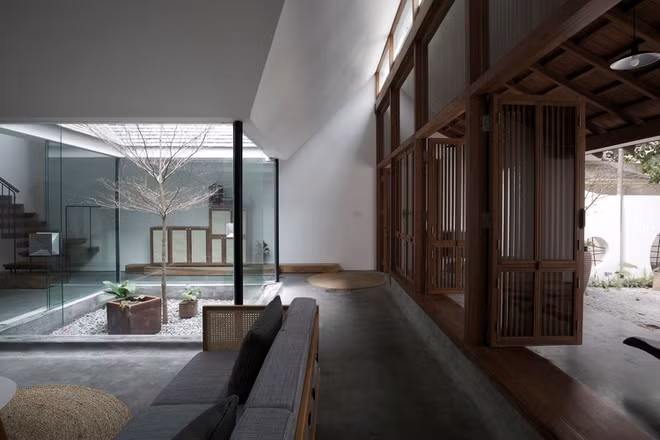 Sau lớp kính ngoài mặt tiền là hệ cửa gỗ truyền thống đã được giản lược chi tiết. Kế đó là phòng khách và “sân trong” của ngôi nhà.