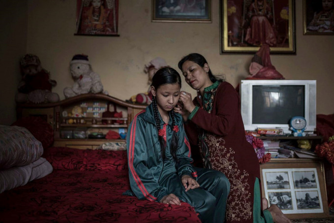 Các Kumari không còn là nữ thần sống “vào ngày mà các cô gái có kỳ kinh nguyệt đầu tiên”, theo bà Contreras Coll. “Trong văn hóa Nepal, máu kinh nguyệt bị cho là ô uế, làm mất sự thiêng liêng. Ngay cả nữ thần cũng bị nhìn nhận khác đi sau khi bắt đầu có kinh nguyệt”. Trong ảnh, mẹ của Unika đeo khuyên tai cho cô gái từng là nữ thần để chuẩn bị đi học. Khi Unika làm Kumari, cha mẹ của em thực hiện nghi lễ pujas mỗi ngày (cúng các vị thần) và tiếp đón các tín đồ đến từ khắp cả nước. Ảnh: Maria Contreras Coll.