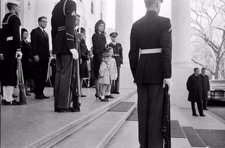 Đệ nhất phu nhân Jacqueline Kennedy cùng hai con đứng ở bậc thềm Nhà Trắng khi quan tài của cố tổng thống được đưa tới Điện Capitol.