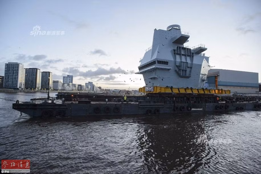 Tháp chỉ huy được sà lan vận chuyển đến điểm lắp ráp. Queen Elizabeth là dự án đóng tàu chiến lớn nhất của Anh từ trước đến nay. Chi phí cho 2 tàu khoảng 6,2 tỷ bảng (khoảng 8,2 tỷ USD). Ảnh: Sina.