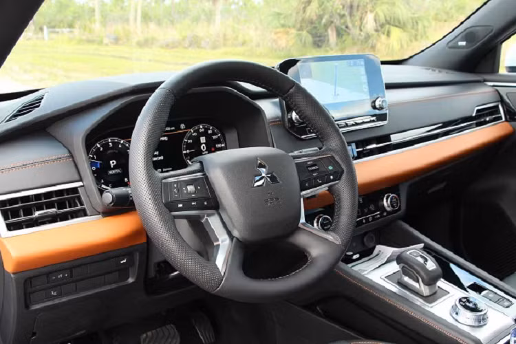 Trên phiên bản SEL Touring được nhắc đến trong bài, hàng ghế lái được bọc da semi-aniline màu đen bóng bẩy, hoàn thiện bởi các đường chỉ khâu màu cam nổi bật. Ngoài ra còn có các chi tiết trang trí bằng da màu cam trải dài ở bệ điều khiển trung tâm, bệ tỳ tay và tấm ốp cửa khiến cho khoang lái càng trở nên cá tính hơn. Mitsubishi Outlander 2022 được trang bị vô-lăng 4 chấu bọc da và mạ bạc khá giống Pajero Sport cho cảm giác cầm lái vừa vặn và tương đối thoải mái. Đó là một trong số ít những thay đổi mà Mitsubishi thực hiện đối với Rogue - một nước đi rất đáng hoan nghênh.