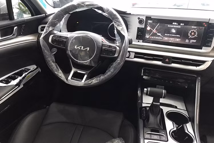 Ở bên trong, Kia K5 GT-Line 2022 mang đến cảm giác thể thao với vô lăng 3 chấu dạng vát đáy, màn hình công cụ kỹ thuật số 12,3 inch nằm phía sau, thiết kế bảng điều khiển trung tâm tập trung về phía người lái,... Toàn bộ khoang cabin của phiên bản GT-Line này được bọc da tông màu đen, ghế lái chỉnh điện đa hướng và tích hợp tính năng sưởi/thông gió.