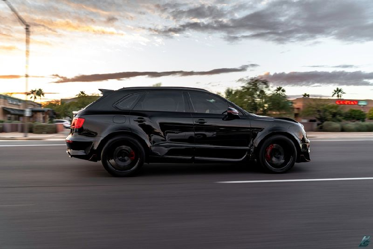 Chiếc SUV siêu sang Bentley Bentayga được hoàn thiện trong lớp sơn đen huyền bí kết hợp với một số điểm nhấn màu đỏ, tạo hiệu ứng thẩm mỹ thú vị. Xe được trang bị mâm xe Onyx 23 inch, bọc gọn trong bộ lốp Continental.