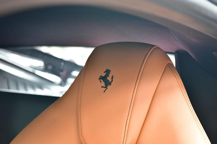 Bên trong khoang lái chiếc siêu xe Ferrari F8 Tributo màu đen đang được chào bán có nội thất bọc màu da bò cùng với các chi tiết bằng nhôm hay carbon, trên tựa đầu ghế ngồi của xe có logo ngựa chồm được thêu bằng chỉ đen, tạo đối lập với bộ ghế màu da bò.