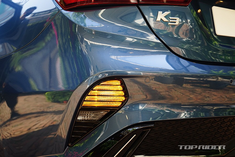 Bên dưới nữa là hốc gió trung tâm cỡ lớn và đi kèm đèn sương mù LED nằm chéo ở 2 góc. Đó là chưa kể đến 2 khe gió hình tam giác ở hai bên góc của cản trước, đi kèm nẹp mạ crôm trang trí, và logo mới của hãng Kia trên nắp ca-pô.