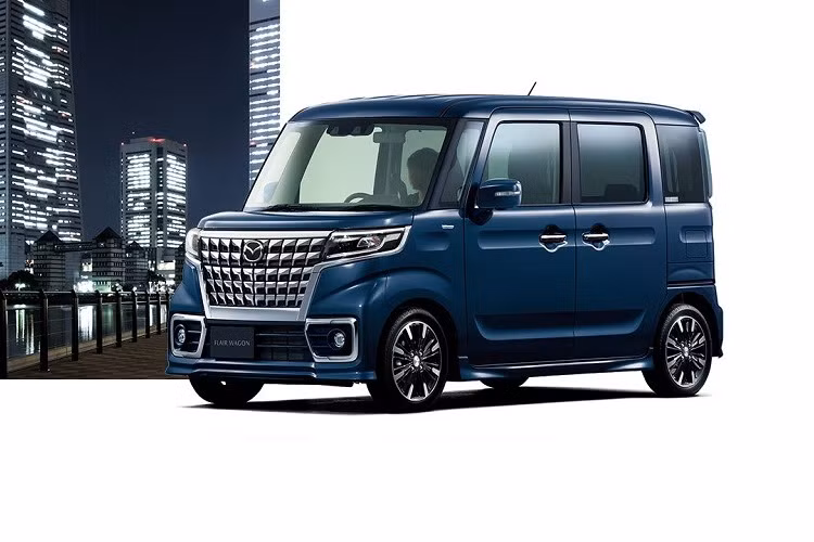 Tiếp đến là hốc gió trung tâm hình thang, đi kèm khung lắp biển số. Ở hai bên hốc gió trung tâm là đèn sương mù trước với viền mạ crôm. Khác với bản thường, Mazda Flair Wagon 2022 bản Custom được trang bị vành la-zăng sơn phối 2 màu thể thao hơn, ốp gương ngoại thất tích hợp đèn báo rẽ và tay nắm cửa mạ crôm. Bên cạnh đó, bản Custom còn có cả cánh gió mui - trang bị vốn không dành cho bản thường.