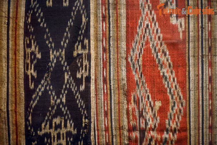  4. Ikat. Trong kỹ thuật ikat hay “nhuộm bao sợi”, người ta dùng xơ vỏ cây hoặc sợi nilon buộc bao xung quanh bó sợi ở những đoạn khác nhau rồi đem nhuộm. Các phần sợi được bao sẽ không bắt màu. Quy trình bao – nhuộm lặp lại nhiều lần để tạo những sợi đa sắc, dùng làm sợi ngang để dệt nên tấm vải ikat. Ảnh: Váy ống áp dụng ikat trên nền đỏ và chàm, người Thái Đen, Điện Biên, 1954.
