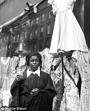 Một phụ nữ da màu đứng trước cửa hàng bán quần áo.