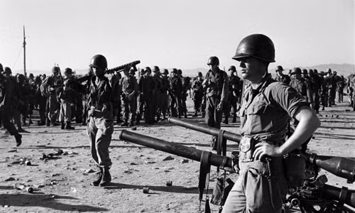 Lính Mỹ đứng cạnh những vũ khí khủng ở bãi biển, được triển khai tại chiến trường Triều Tiên.