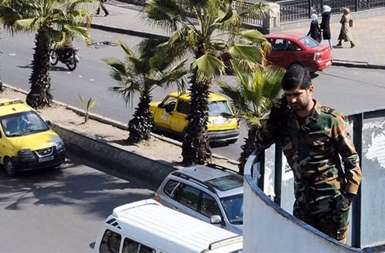 Một binh sỹ chính phủ Syria nghe điện thoại trên sảnh ban công có hướng nhìn xuống một con đường yên ả ở đất nước Trung Đông bị chiến tranh tàn phá này.