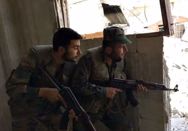 Hai binh sỹ chính phủ Syria nấp sau bức tường trong lần giao chiến.